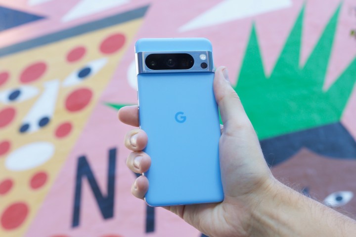 Cineva tine Google Pixel 8 Pro in fata unei picturi murale colorate.