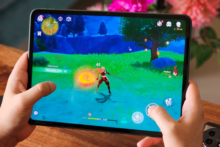 Genshin Impact ruleaza pe OnePlus Pad cu o masa de lemn si flori false in fundal.